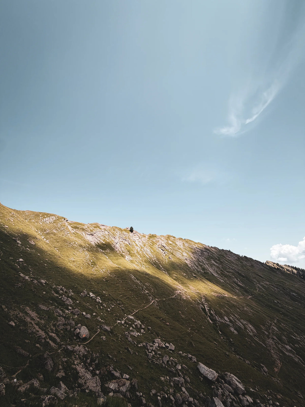 Sonniger Berghang mit einem Pfad unter blauem Himmel
