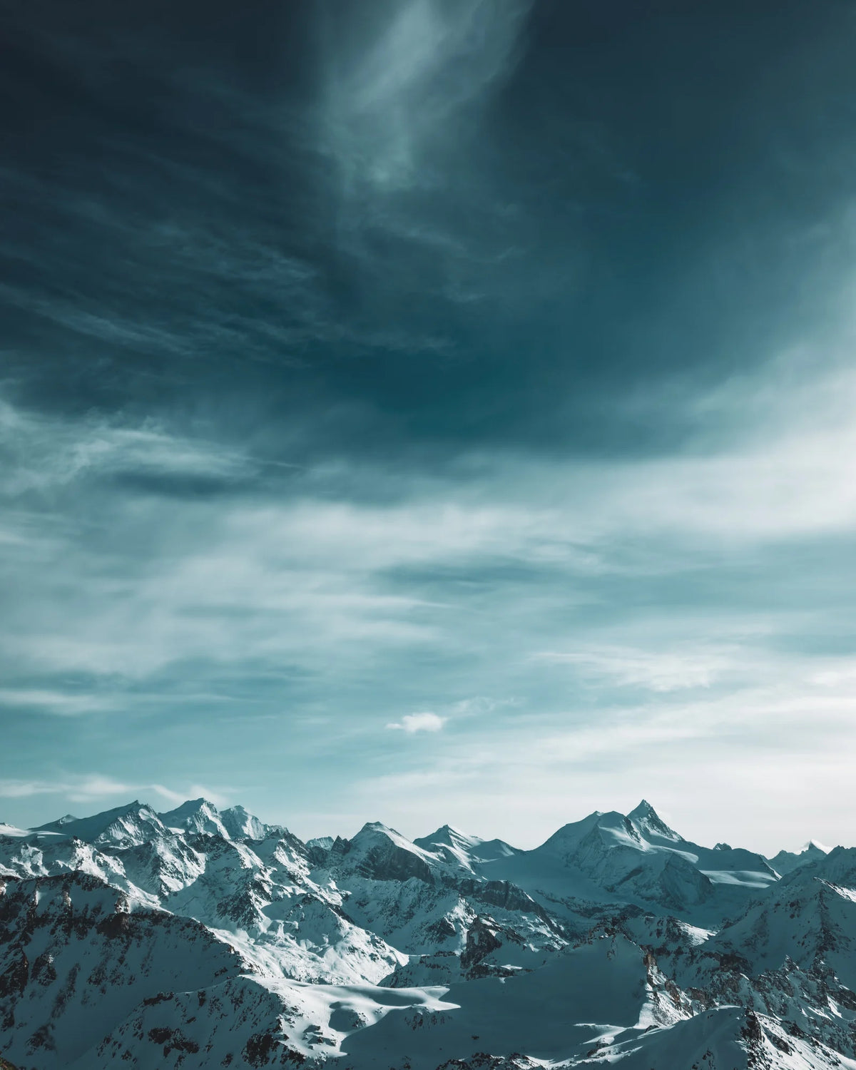 Verschneite Gipfel unter einem Himmel mit Schleierwolken