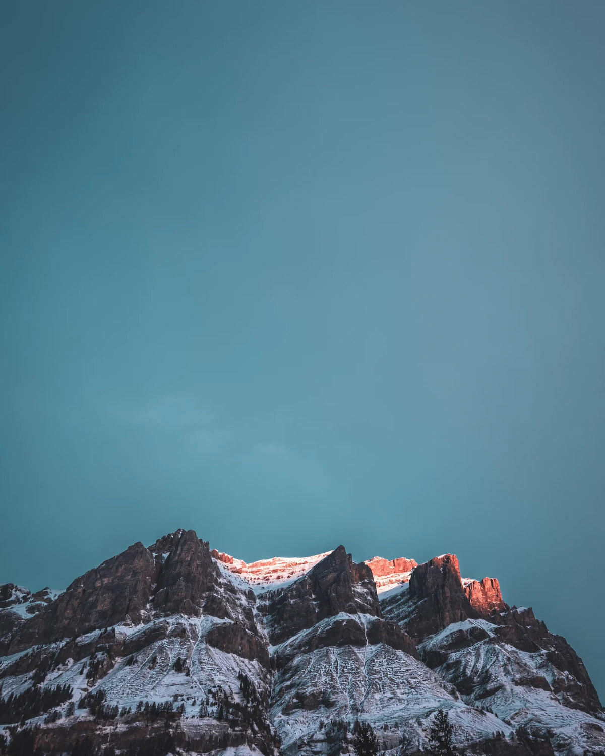 Felsgrat mit Schnee, die oberste Kante im letzten Licht, darüber ein leerer blauer Himmel